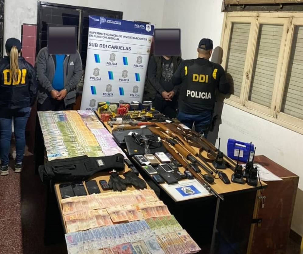 Los aprehendidos frente a una mesa llena de armas y dinero. 